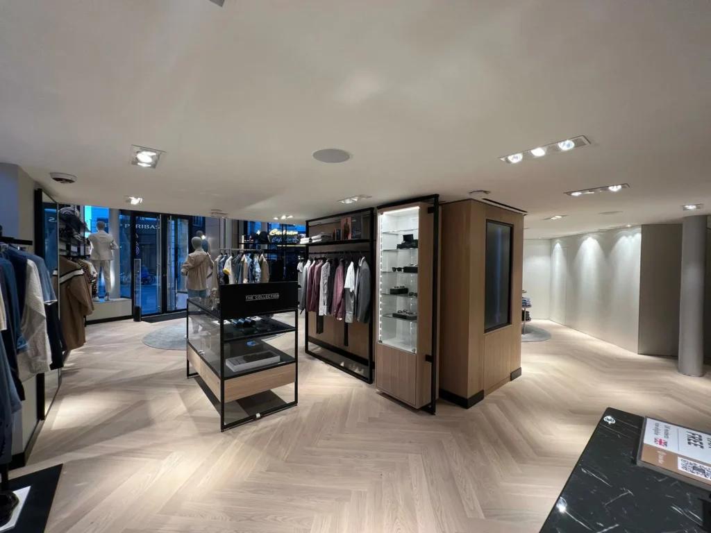 Vue grand angle d’une boutique BOSS avec linéaires textile, mobilier noir et éclairage intégré
