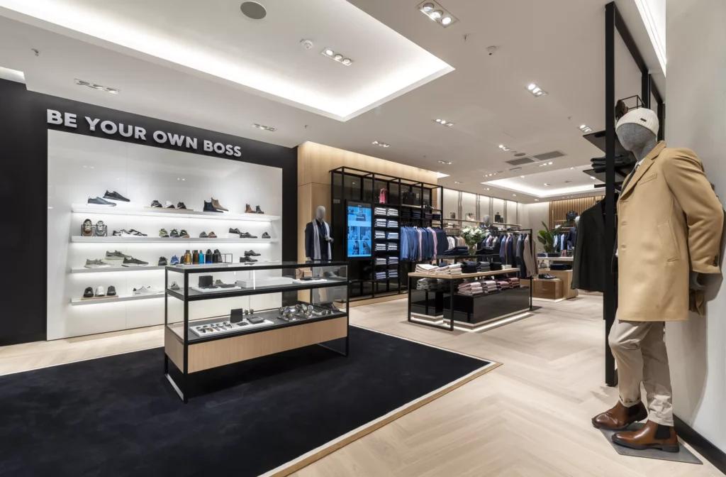 Vue grand angle de la boutique BOSS Parly 2 avec linéaires chaussures, mobilier central et éclairage intégré