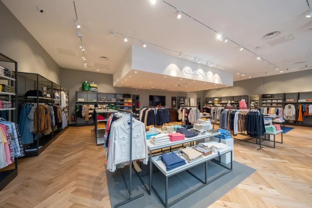 Vue grand angle d’une boutique GANT avec parquet, portants vêtements, tables de présentation et éclairage retail