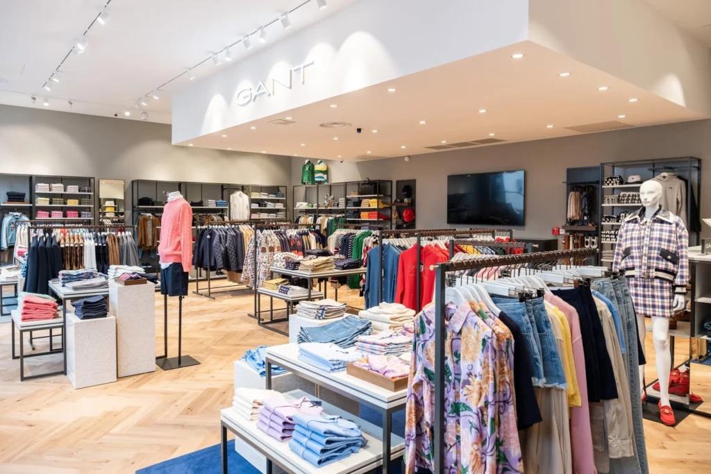Espace de vente GANT avec signalétique lumineuse, vêtements sur portants et mobilier central