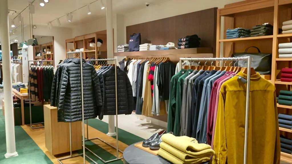 Rayons vêtements GANT avec mobilier bois, portants métalliques, pulls pliés et espace prêt-à-porter