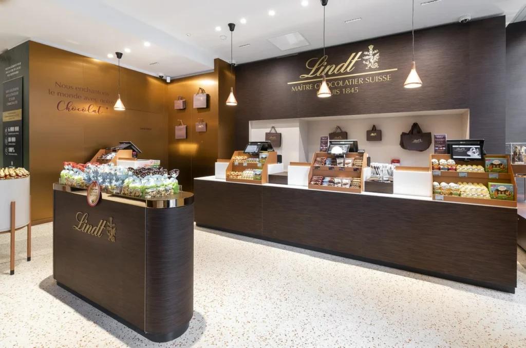 Espace de vente du flagship Lindt Paris Opéra avec comptoirs, mobilier bois et signalétique Lindt