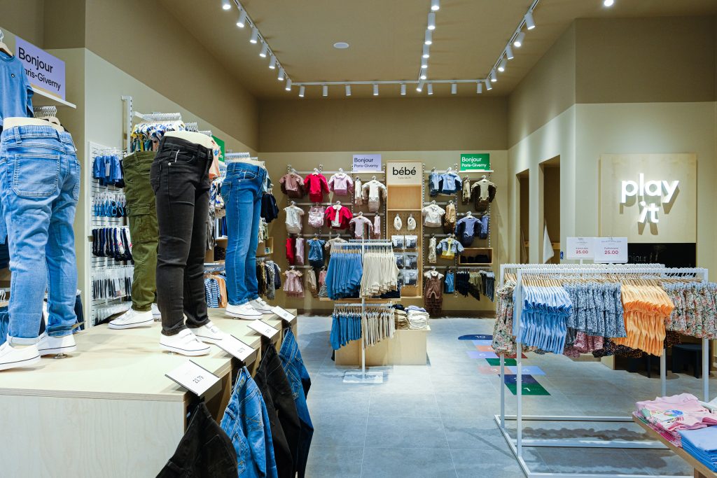 Intérieur de la boutique Name It Giverny avec mobilier retail, collections enfant et parcours client fluide