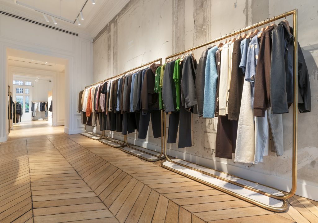 Portants dorés de vêtements dans la boutique Sandro Paris Victor Hugo avec mur brut et parquet en chêne