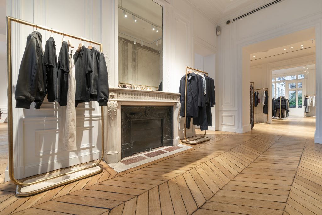 Cheminée ancienne dans la boutique Sandro Paris Victor Hugo avec portants dorés et parquet en chêne
