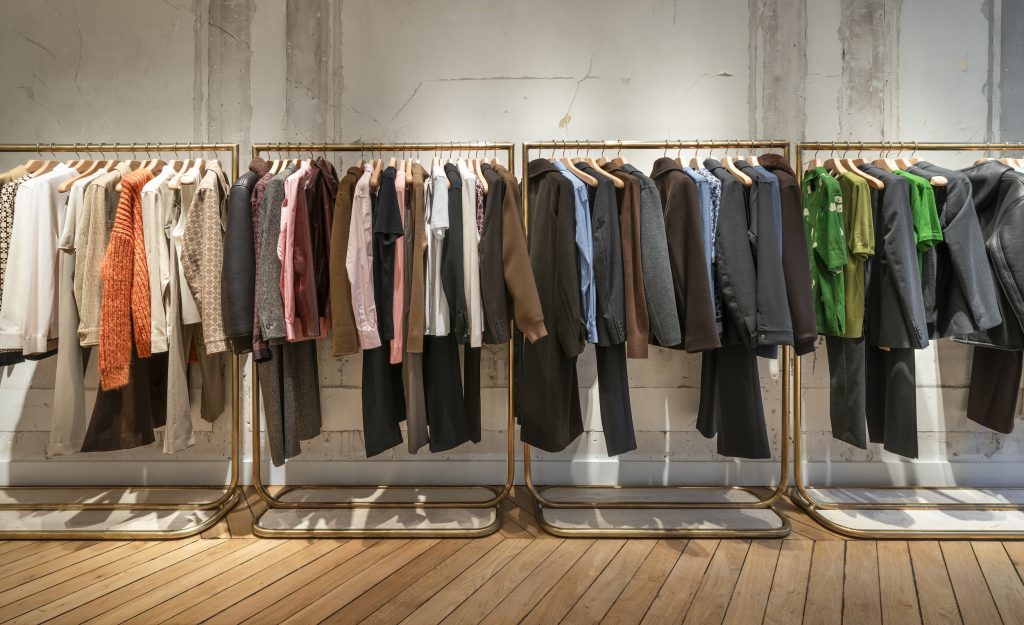 Linéaires de vêtements Sandro dans la boutique Paris Victor Hugo avec portants dorés et mur effet brut