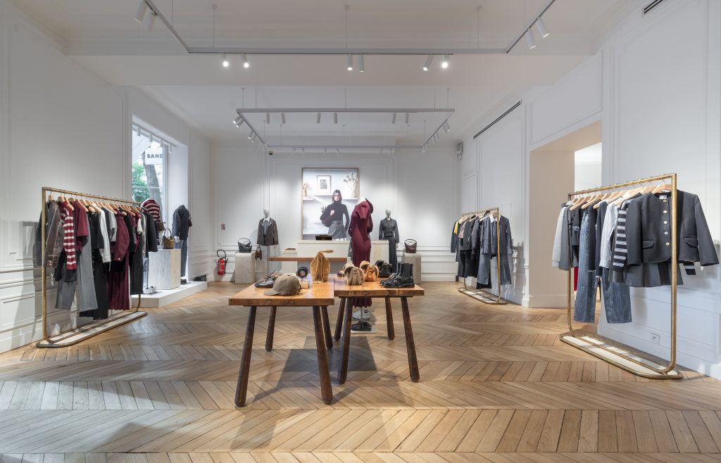 Intérieur de la boutique Sandro avenue Victor Hugo à Paris avec parquet en pointe de Hongrie, mobilier retail et portants dorés