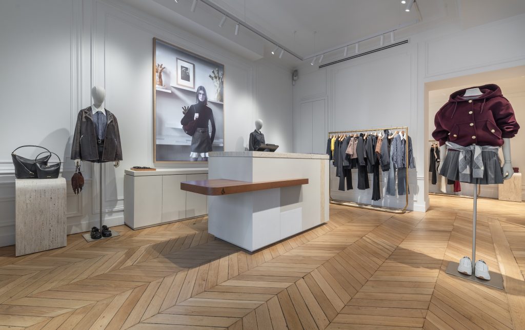 Vue globale de la boutique Sandro Paris Victor Hugo avec tables de présentation, portants dorés et parquet en chêne