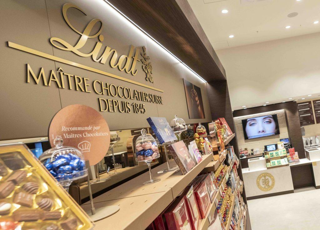 Îlots centraux de chocolats Lindt dans la boutique Cap 3000 avec mobilier arrondi et produits colorés