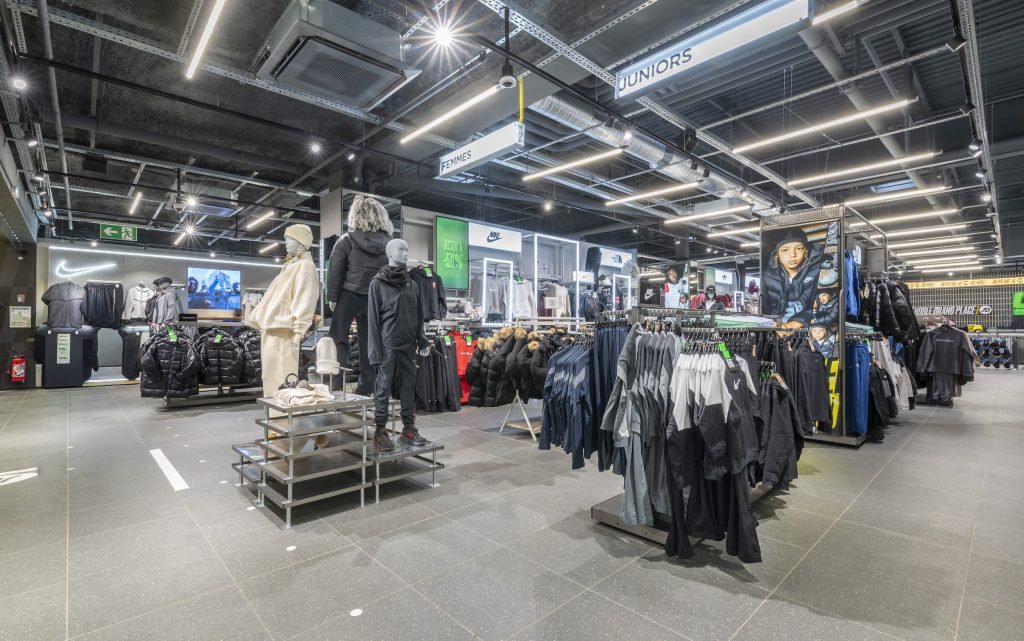 Espace textile JD Sports Grenoble avec portants, mannequins, signalétique femmes et juniors