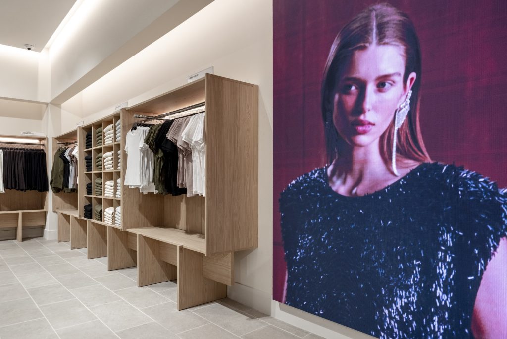Visuel de campagne H&M Rosny avec rayons prêt-à-porter, mobilier bois et éclairage retail