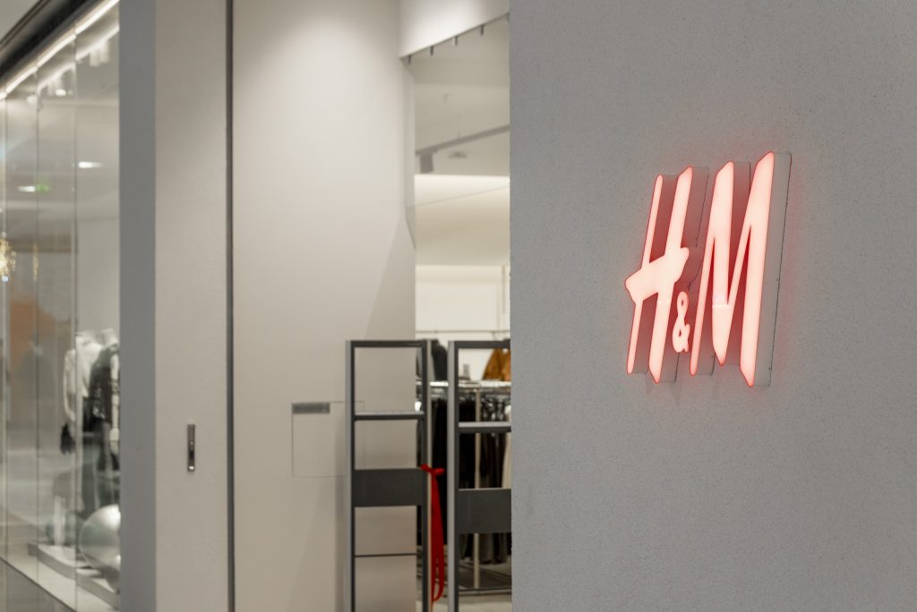 Logo lumineux H&M dans le magasin de Rosny avec mur texturé et entrée vers l’espace de vente