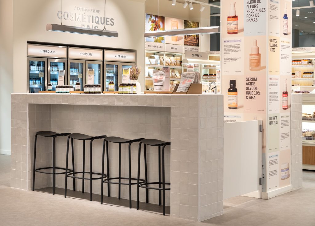 Espace cosmétiques frais Aroma-Zone Vélizy avec vitrines réfrigérées, comptoir carrelé et tabourets noirs