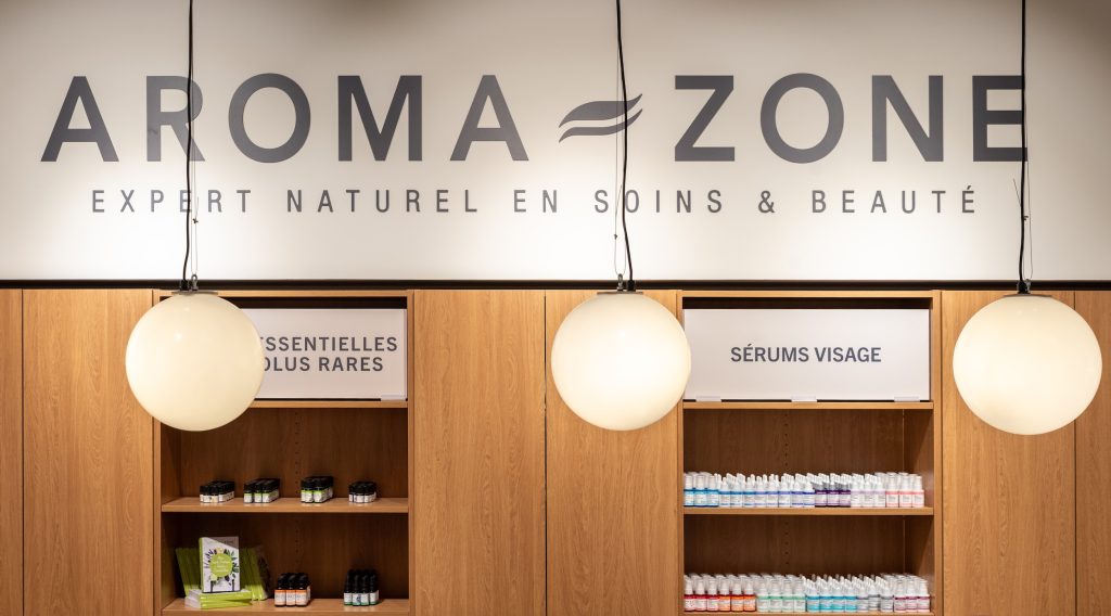 Logo mural Aroma-Zone dans la boutique Vélizy avec linéaires bois, suspensions lumineuses et produits beauté