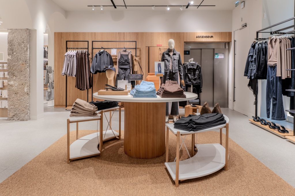 Espace central de la boutique MANGO Lyon avec table ronde, mannequins, portants et habillage mural bois