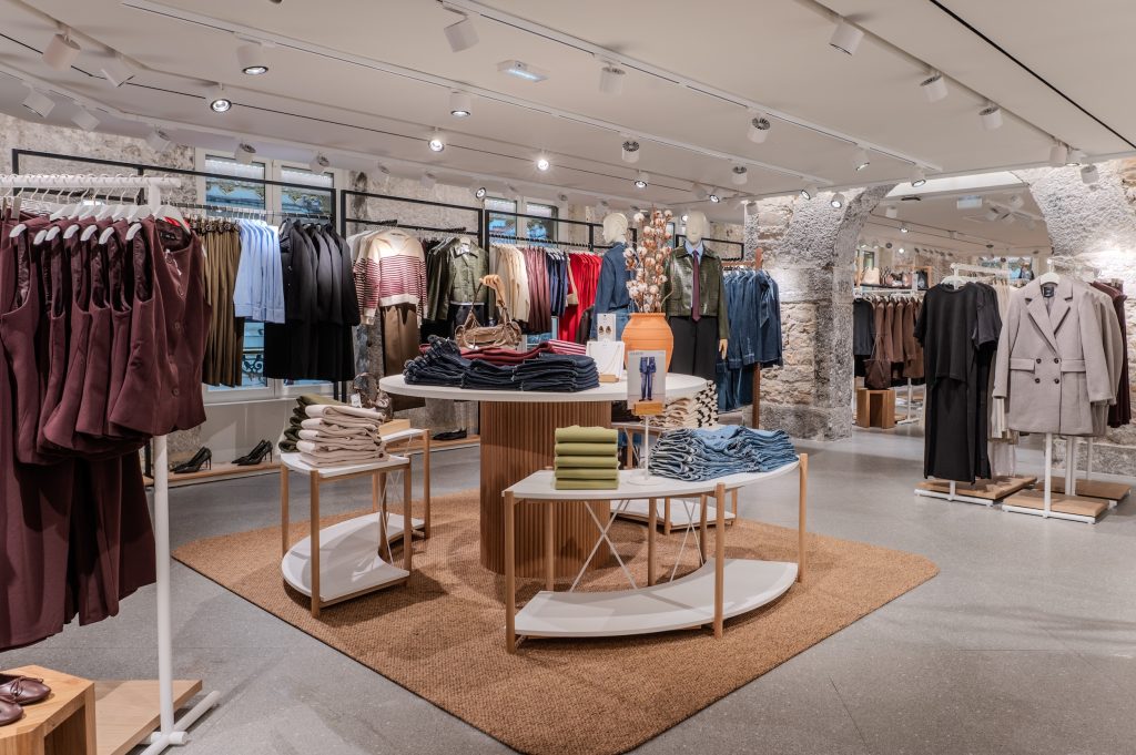 Vue globale de la boutique MANGO Lyon République avec îlot central, collections mode, murs en pierre et éclairage