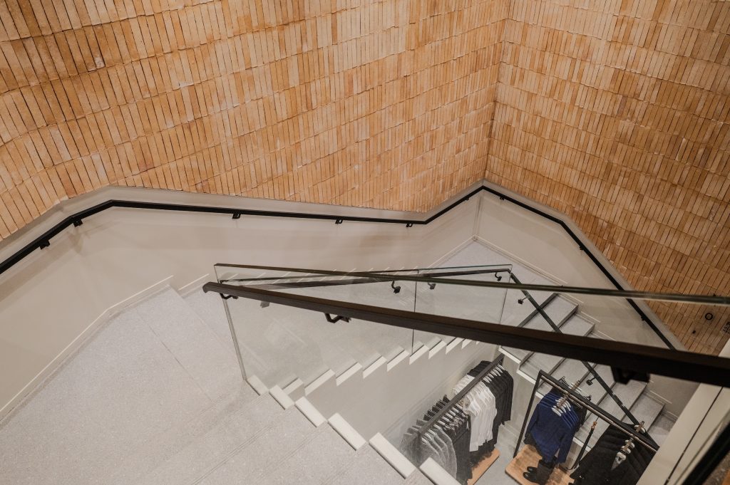 Escalier de la boutique MANGO Lyon avec garde-corps vitré et habillage mural bois en briques