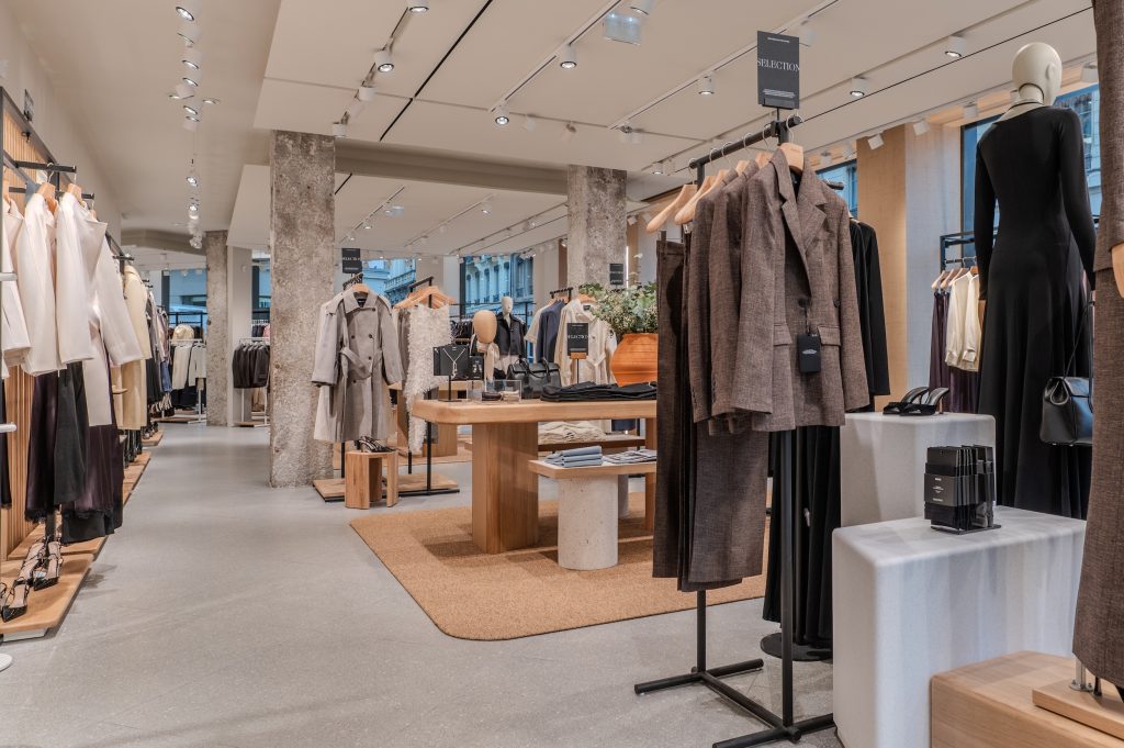 Vue intérieure de la boutique MANGO Lyon République avec portants, mobilier bois, murs en pierre et éclairage retail