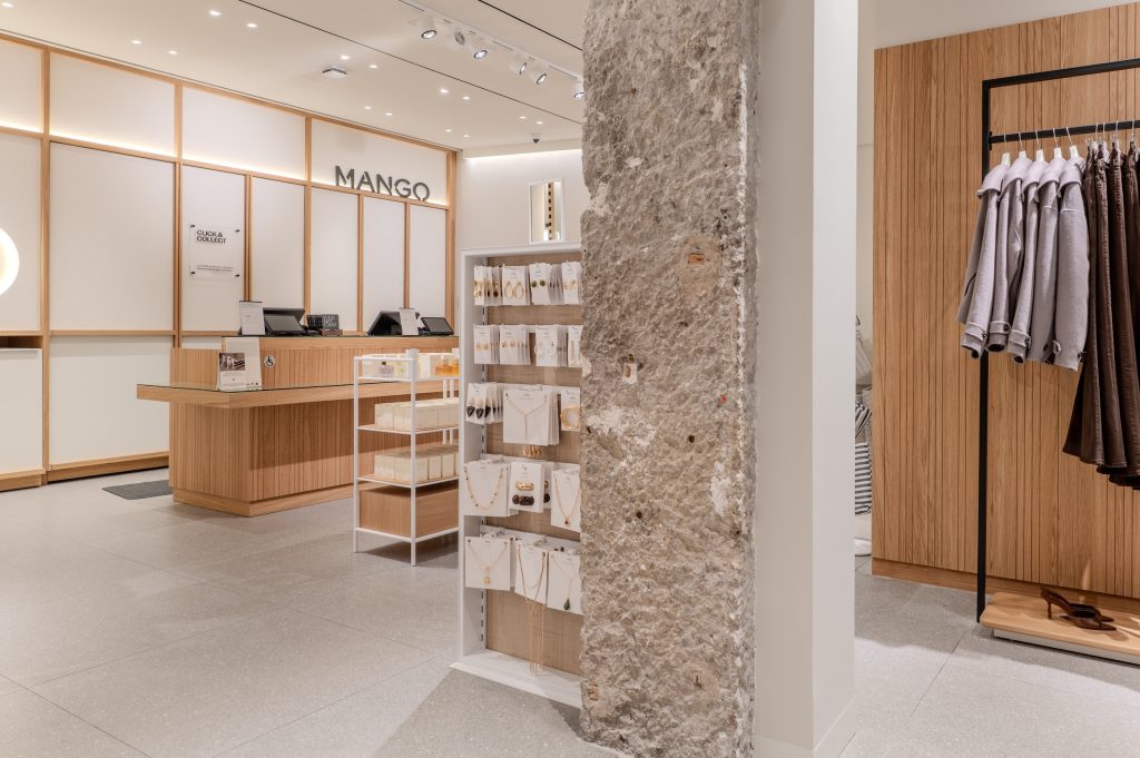 Espace caisse de la boutique MANGO Lyon avec comptoir bois, logo mural et mur en pierre conservé