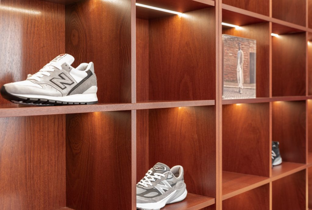 Linéaires de sneakers New Balance dans la boutique Lyon avec étagères bois, structure métallique et éclairage intégré