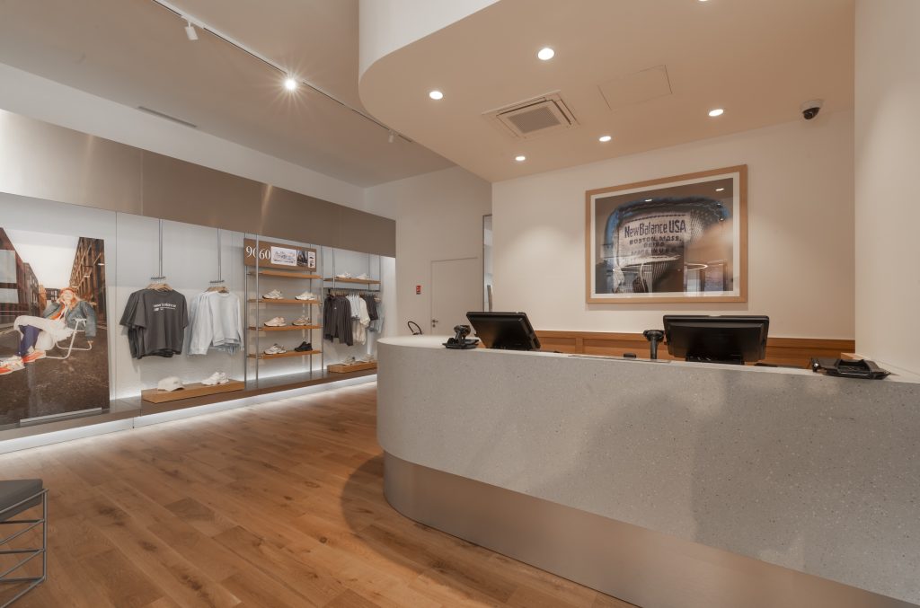 Espace caisse de la boutique New Balance Lyon avec comptoir minéral, parquet bois et linéaires produits