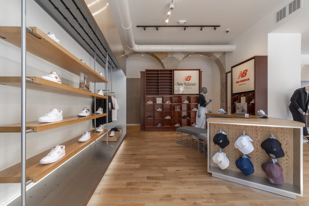 Vue globale de la boutique New Balance Lyon avec mur sneakers, mobilier central, arches et parquet bois