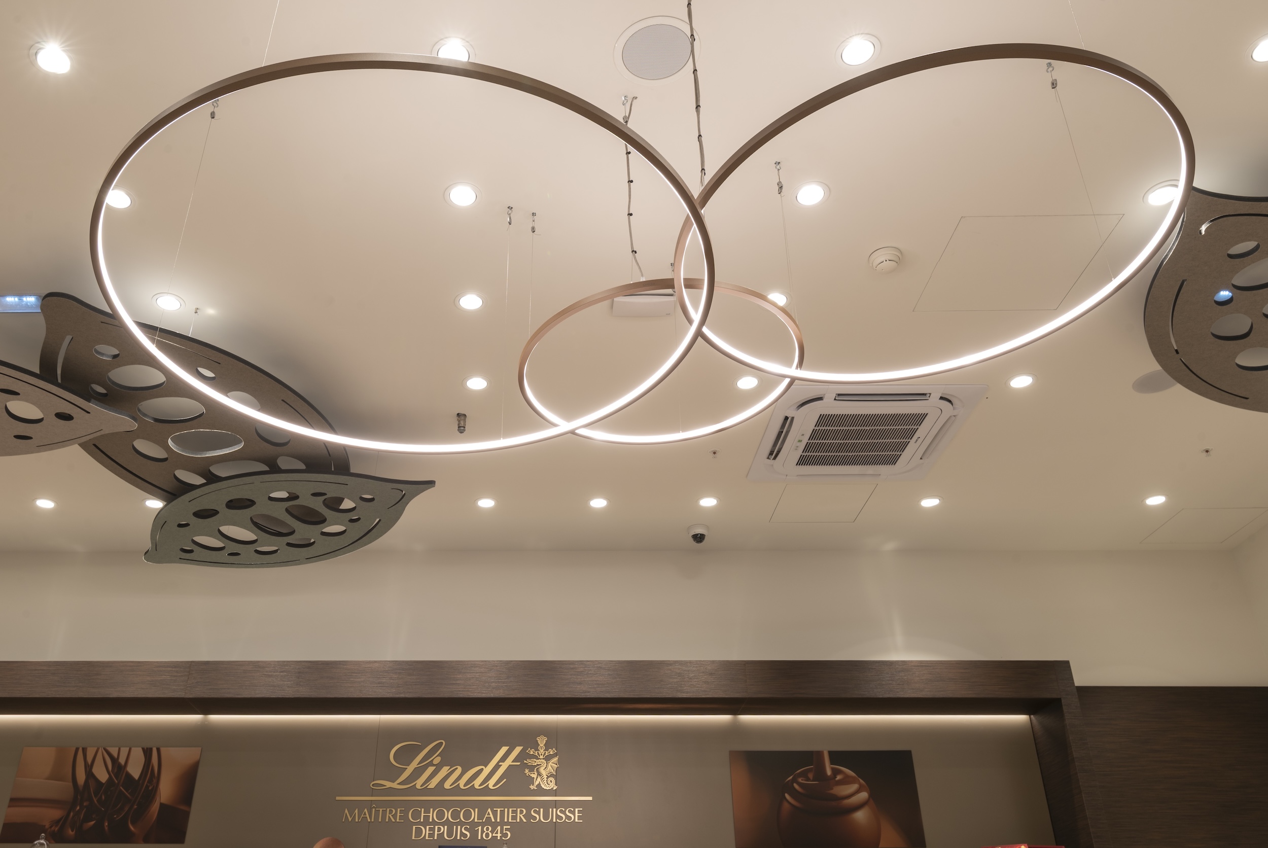 Luminaires circulaires et plafond décoratif dans la boutique Lindt rénovée à Nailloux