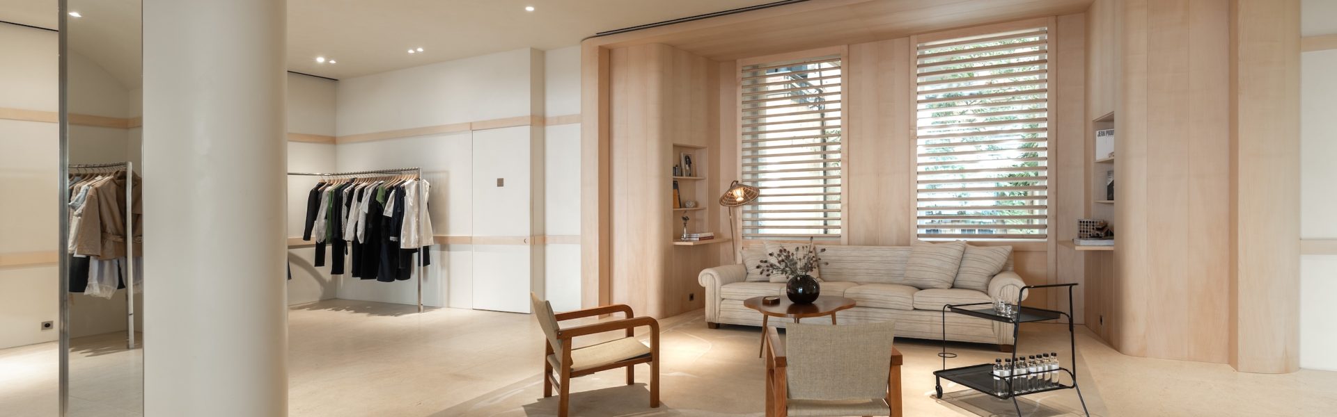 Espace salon Frame Cannes avec canapé, fauteuils, portants vêtements et finitions bois clair