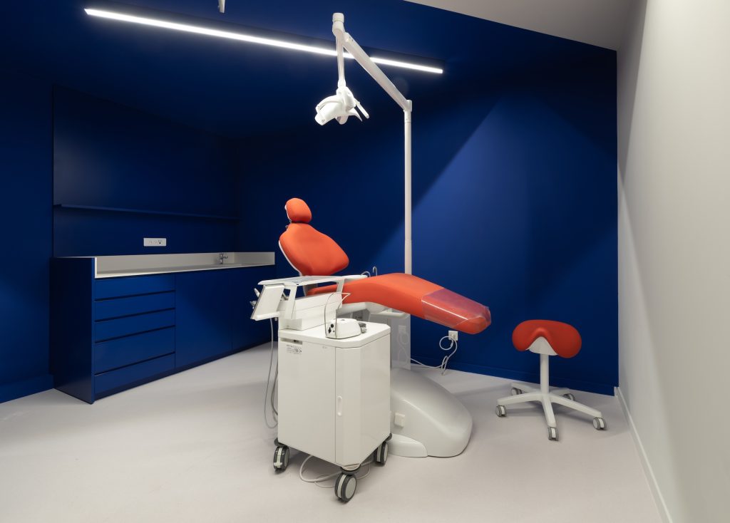 Salle de soin du cabinet dentaire Smile2Impress Lille avec fauteuil dentaire rouge, murs bleus et éclairage technique