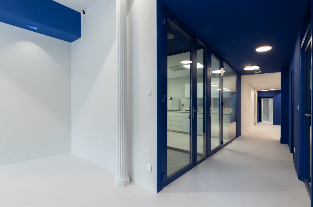 Couloir du cabinet Smile2Impress Lille avec cloisons vitrées, portes bleues et espaces techniques