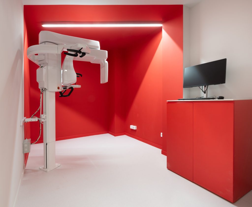 Salle de radiologie du cabinet Smile2Impress Lille avec équipement médical, mur rouge et mobilier technique