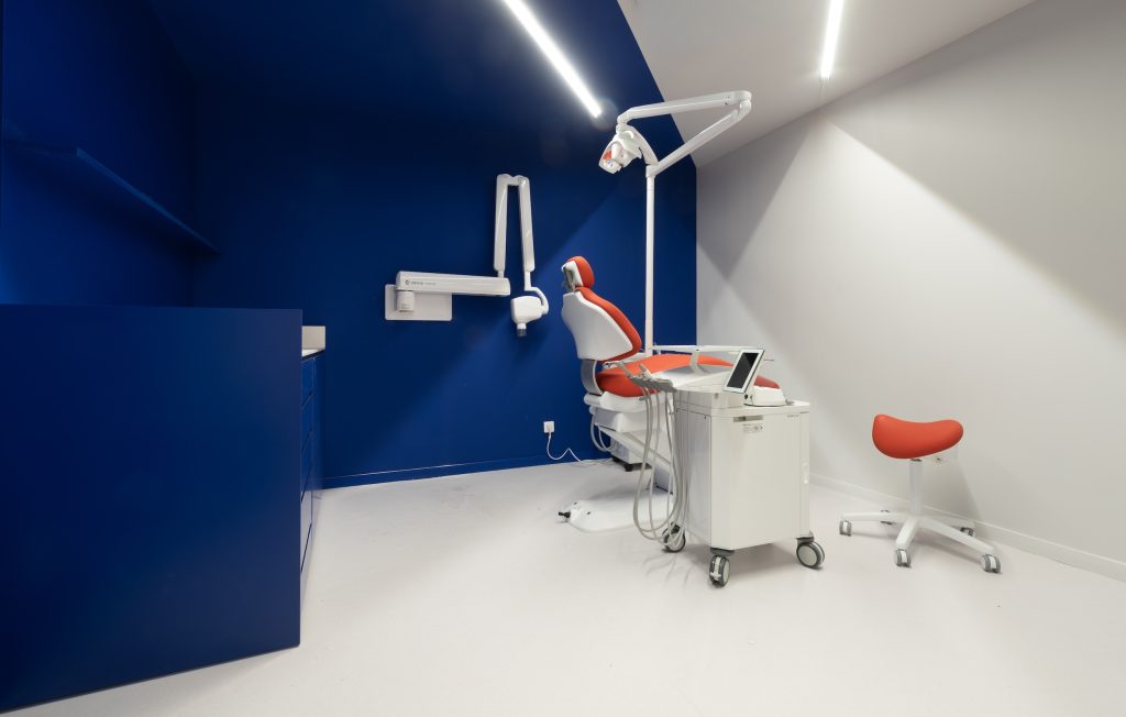 Salle de consultation dentaire Smile2Impress Lille avec fauteuil rouge, murs bleus et mobilier médical intégré