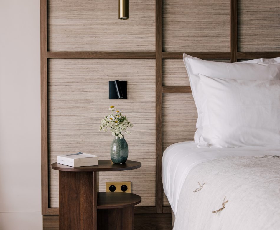 Tête de lit bois, table de chevet et linge clair dans une chambre de l’hôtel Les Bassans