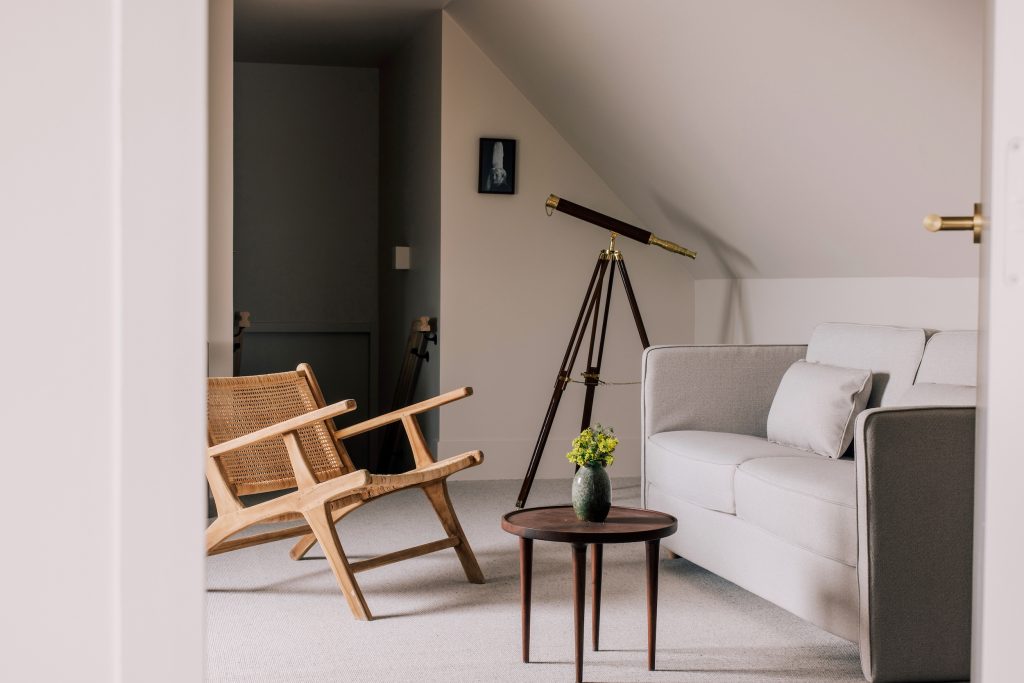Salon de l’hôtel Les Bassans avec fauteuil bois, canapé clair, table basse et télescope