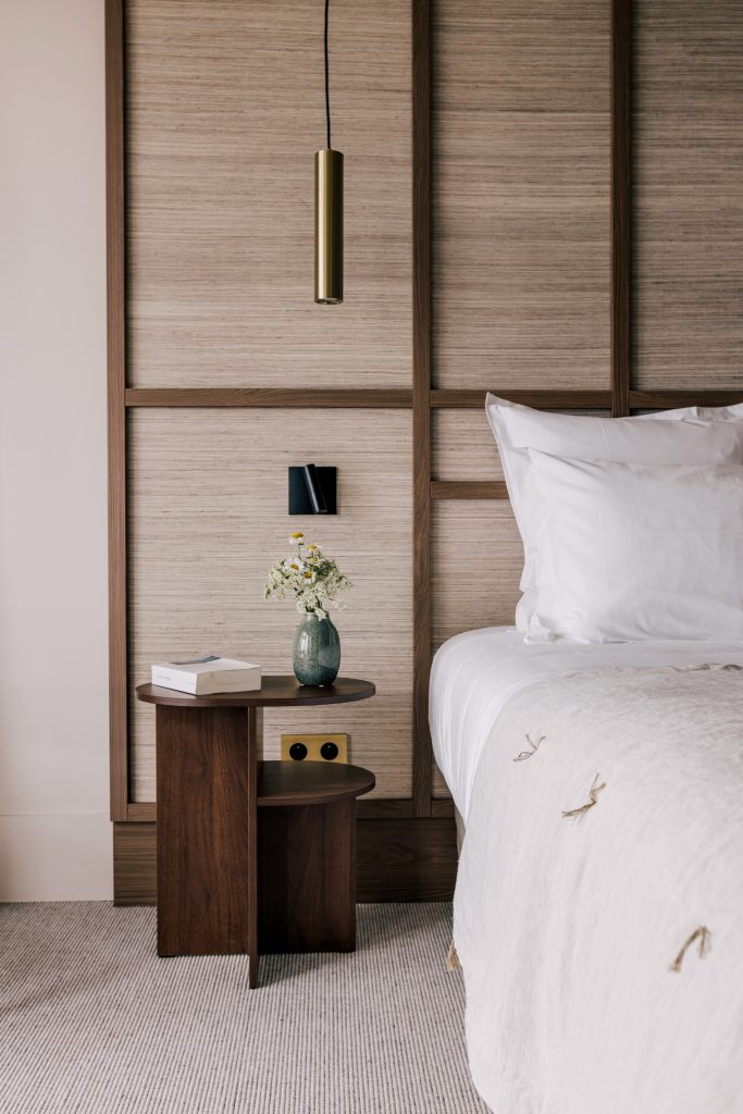 Détail de chambre rénovée à l’hôtel Les Bassans avec tête de lit bois, table de chevet et linge clair