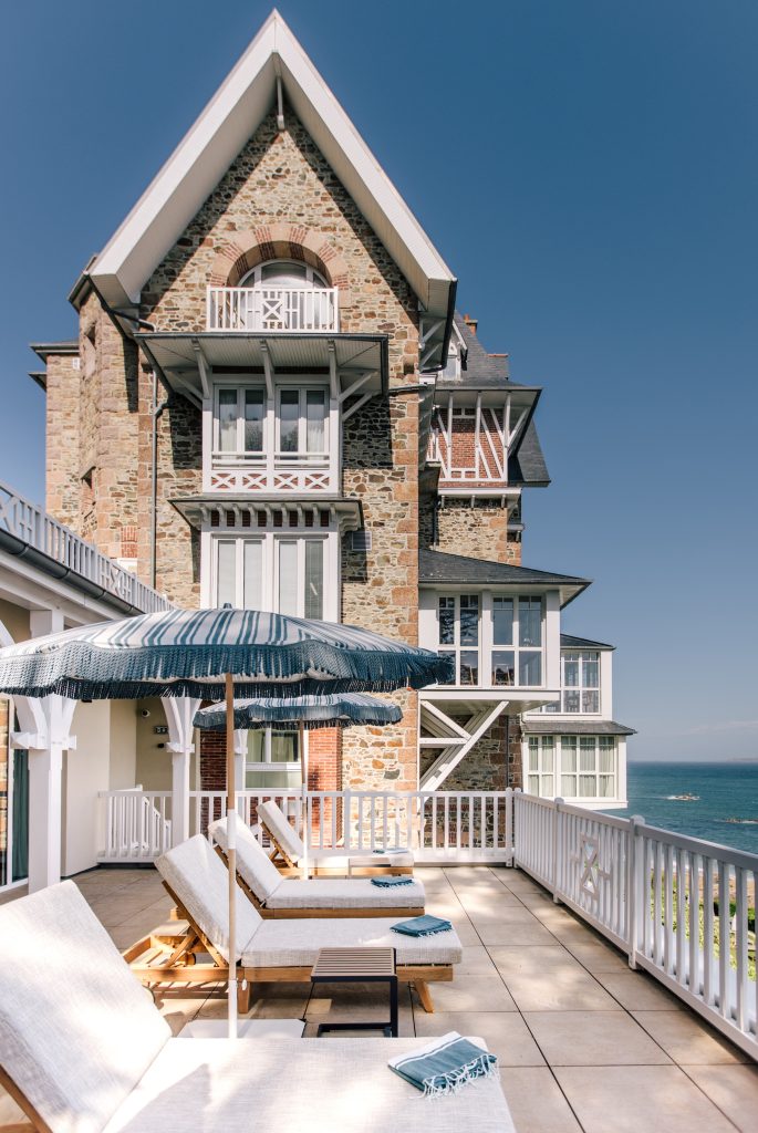 Terrasse de l’hôtel Les Bassans avec transats, parasols et façade bretonne face à la mer