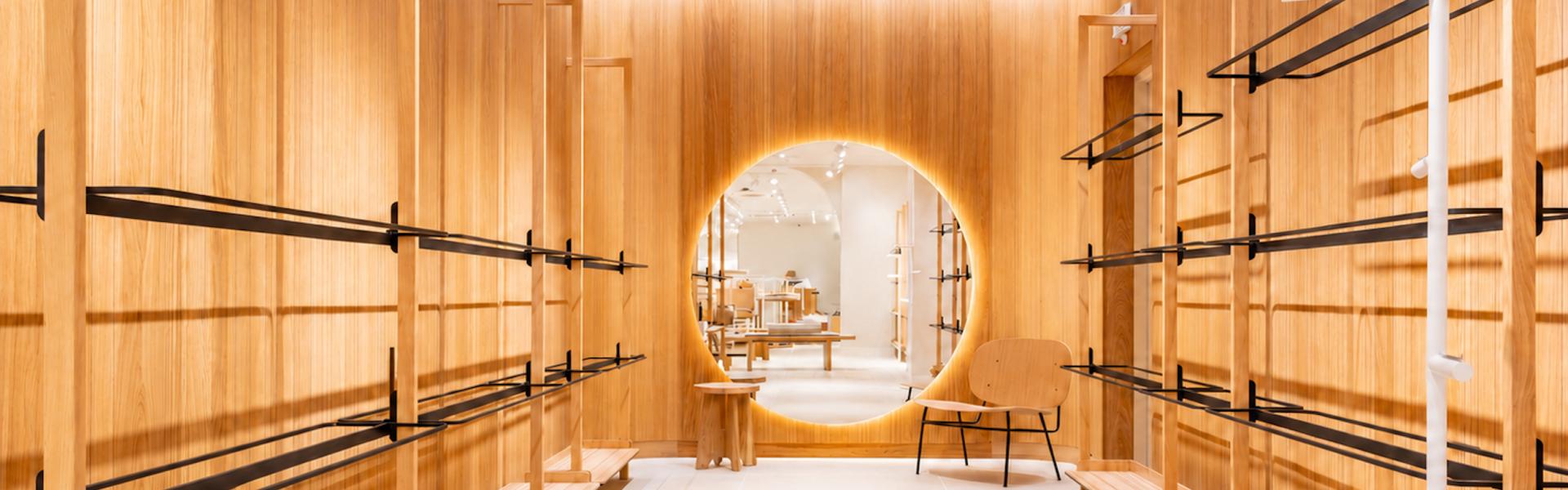 Boutique Mango Caen New Med avec revêtements bois, portants vêtements noirs et miroir rond lumineux