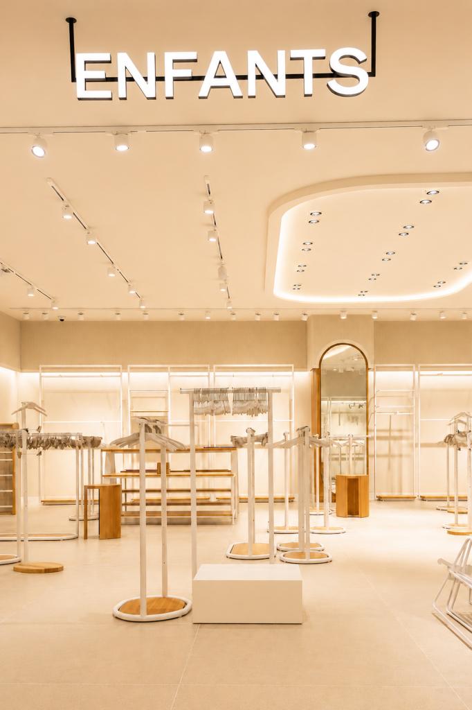 Espace enfants de la boutique Mango Caen New Med avec portants blancs, mobilier bois et éclairage intégré