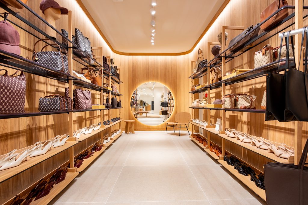 Espace maroquinerie de la boutique Mango Caen avec étagères bois, sacs, chaussures et miroir rond