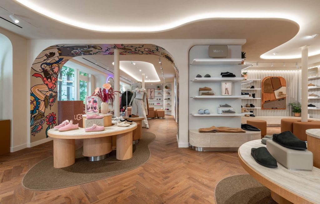 Boutique UGG Le Marais avec arche décorative, tables produits, plafond courbe lumineux et linéaires chaussures