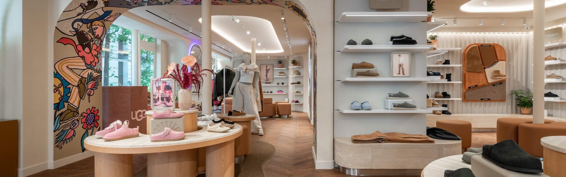 Boutique UGG Le Marais avec arche décorative, tables produits, plafond courbe lumineux et linéaires chaussures