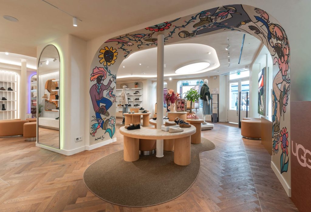 Table centrale de la boutique UGG Le Marais avec arche illustrée, miroir lumineux, parquet en chevrons et espaces produits