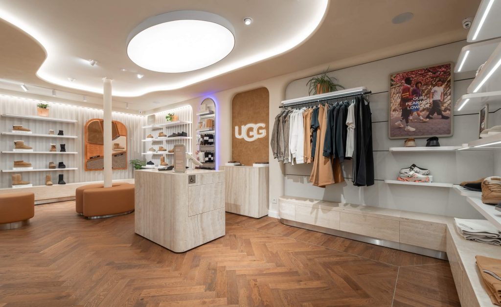 Boutique UGG Le Marais à Paris avec mobilier clair, plafond courbe lumineux, portants vêtements et espace chaussures