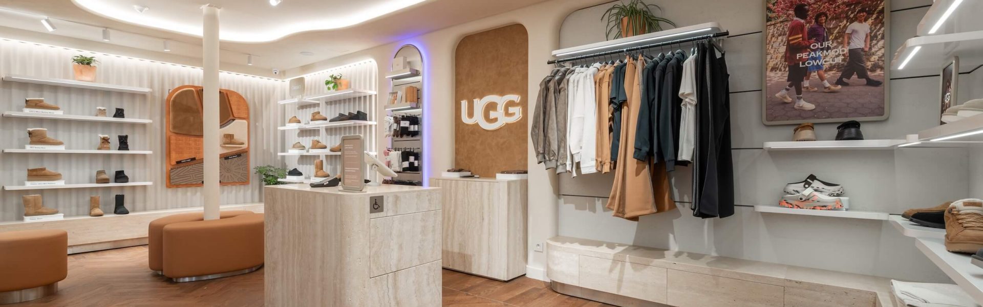 Boutique UGG Le Marais à Paris avec mobilier clair, plafond courbe lumineux, portants vêtements et espace chaussures