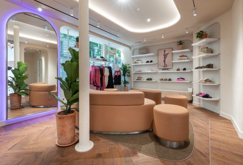 Espace lounge de la boutique UGG Le Marais avec assises arrondies, miroir lumineux, plantes et étagères produits