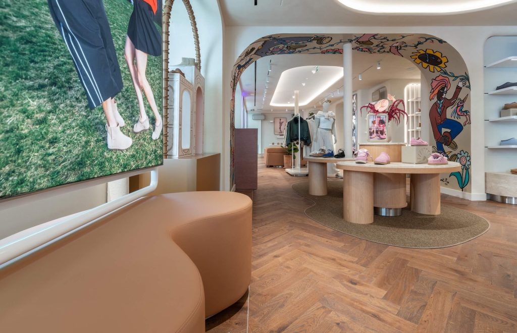 Boutique UGG Le Marais avec arche illustrée, table centrale, écran digital et parquet en chevrons