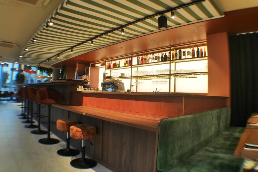 Bar avec étagères rétroéclairées, banquette verte et plafond rayé du restaurant Jordan Tomas Pizza à Nantes